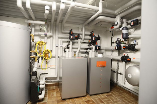 Ein Wärmepumpe und mehrere Rohre, die von der Wärmepumpe wegführen und an der Decke des Raums verlaufen. 